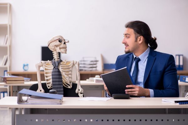 A young male employee with skeletons in the office.